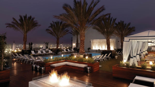 The rooftop of The London West Hollywood at Beverly Hills, pictured at night, features a fire pit and palm trees.