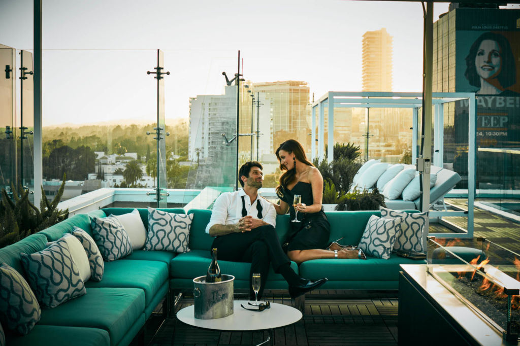 A couple sits on a teal sofa on the rooftop of The London Hotel, West Hollywood, CA.