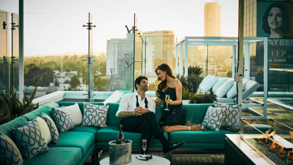 A couple sits on a teal sofa on the rooftop of The London Hotel, West Hollywood, CA.