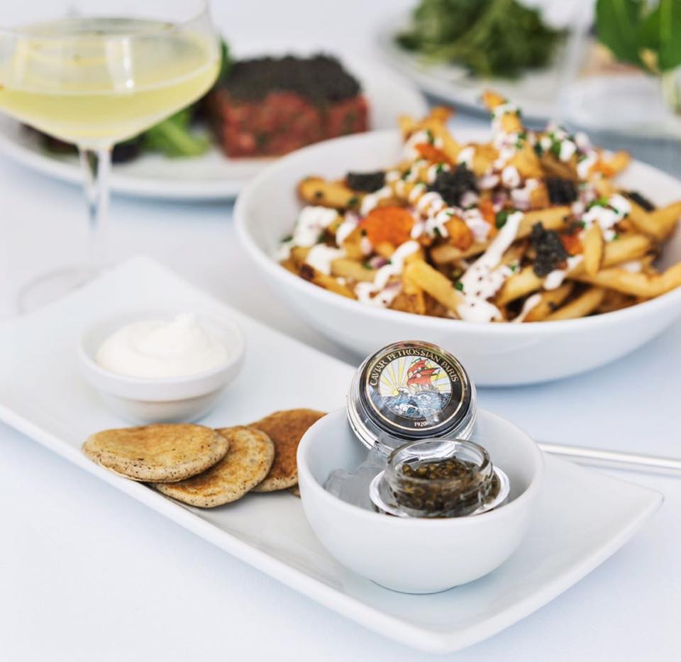 Caviar and champaign sits on a table with a white tablecloth at Petrossian in West Hollywood.