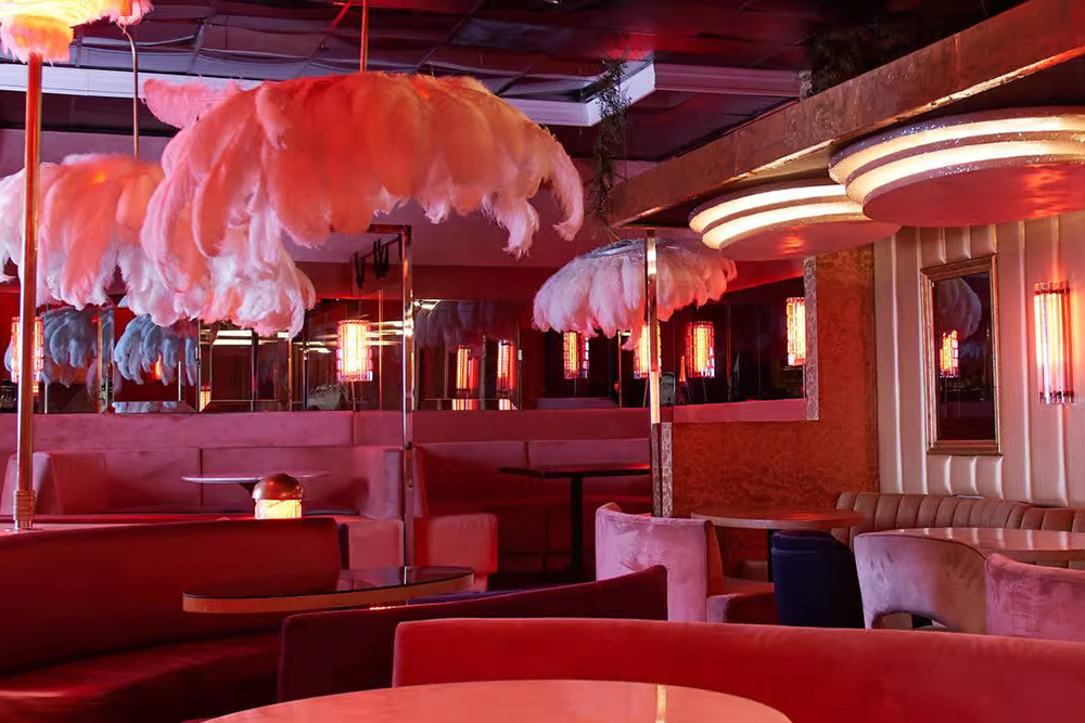 Interior of The Classic Cat LA, with pink banquette seating and pink feather plumes hanging from the ceiling. West Hollywood, CA.