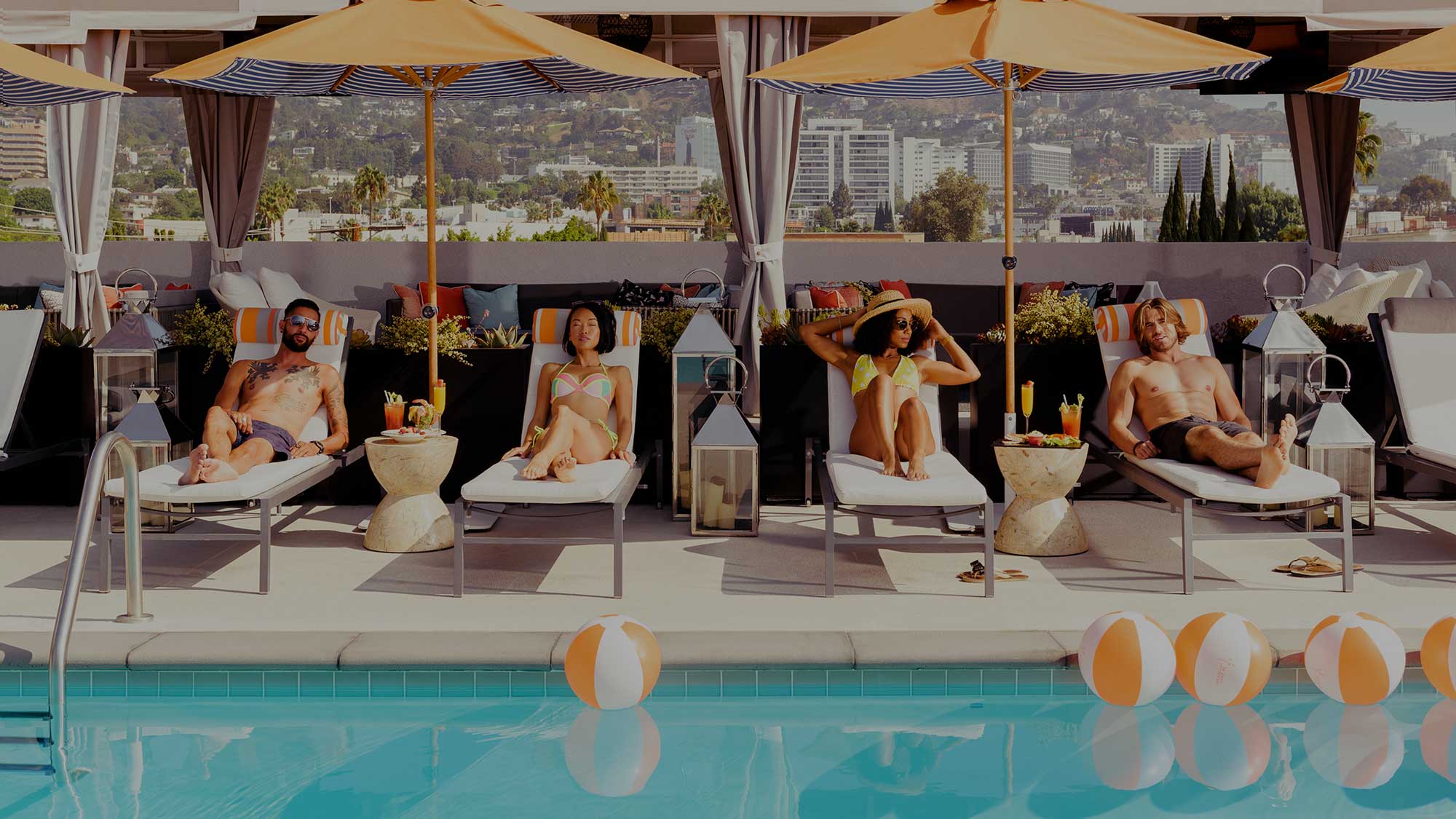 Two women lounge on chairs next to a pool in West Hollywood, California