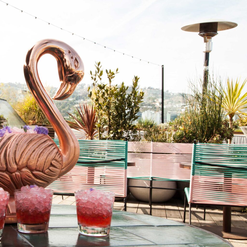 A rooftop is pictured with a pink flamingo sculpture and a pink cocktail in the foreground. E.P. & L.P., West Hollywood, California.