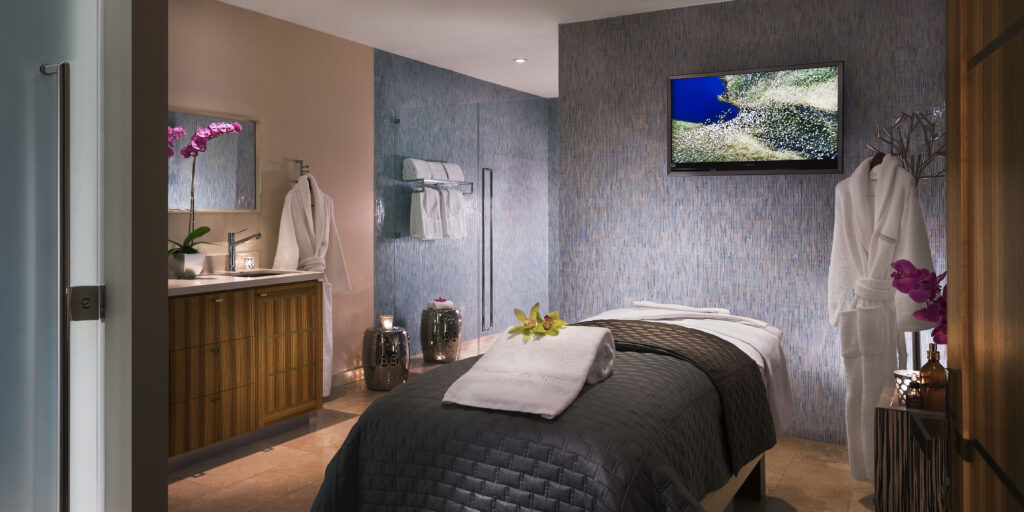 Massage treatment room at the SPA at Sunset Marquis. The room is a mix of beige, blue and purple decor and furnishings, providing a relaxing setting.