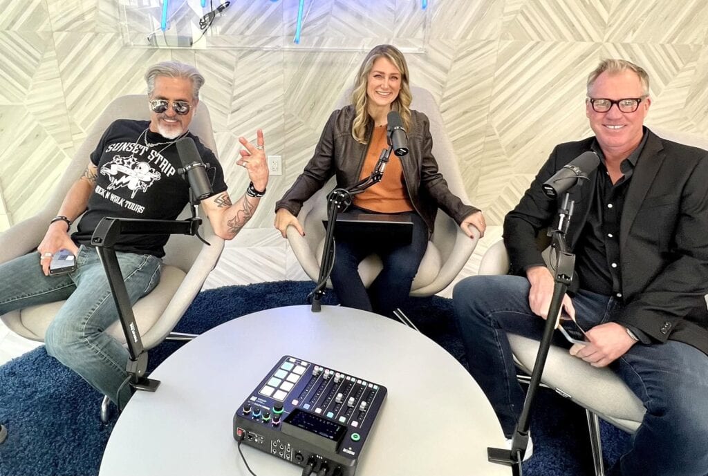 Three people sit around a table with microphones and audio equipment, preparing for a podcast or radio recording in a modern studio.