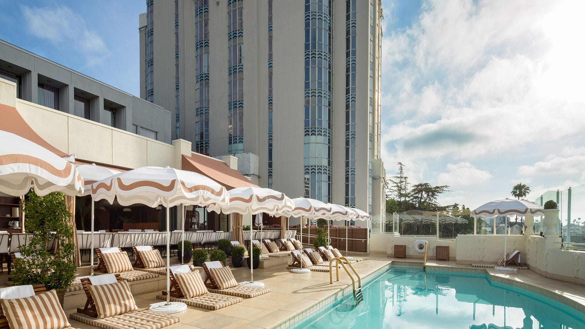 The rooftop pool at the Sunset Tower Hotel in West Hollywood, California, featuring lounge chairs and white umbrellas.