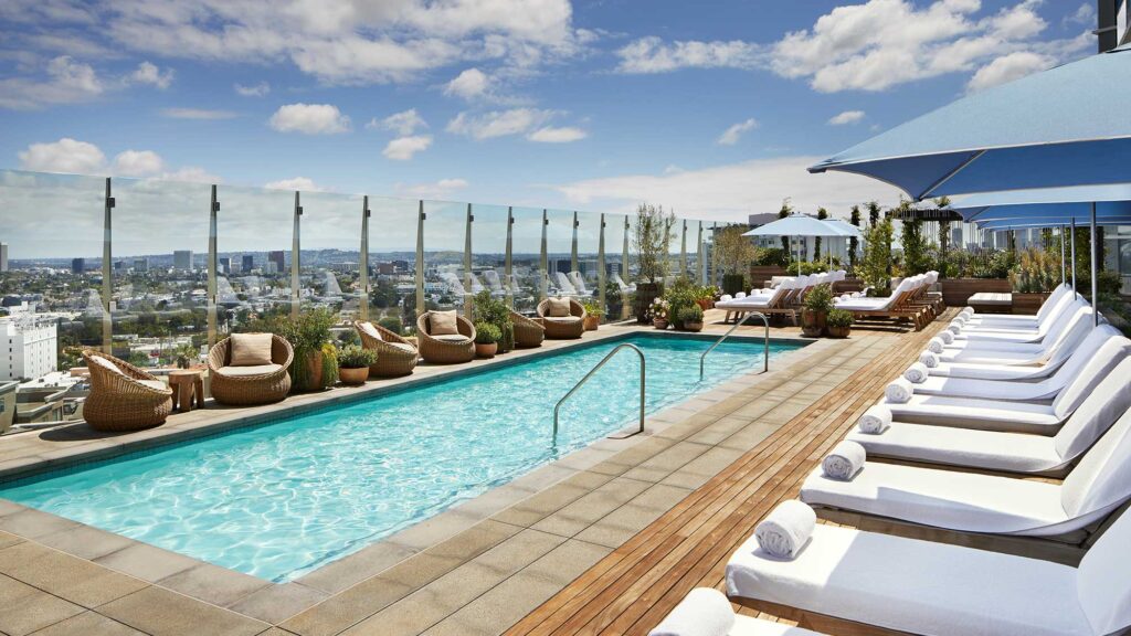 The rooftop pool at 1 Hotel West Hollywood, with white lounge chairs and glass walls offering expansive views of Los Angeles.