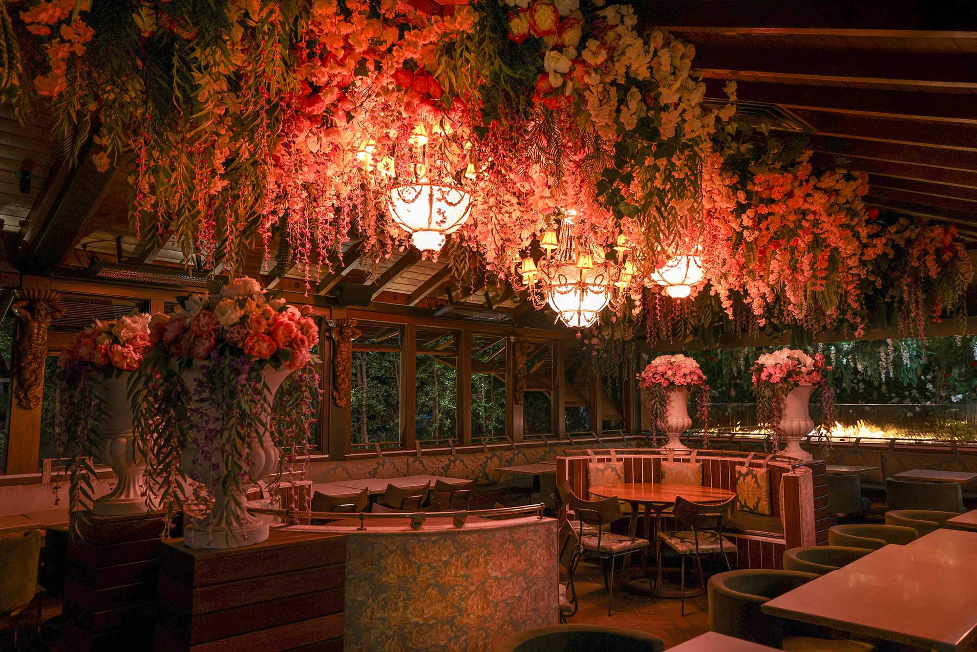 A dimly lit restaurant dining room features bunches of flowers hanging from the ceiling. Arden, West Hollywood, California.