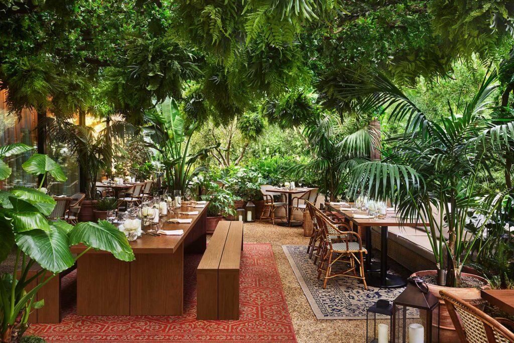 The open-air patio at Ardor restaurant, featuring rugs, bench seating and lush foliage. West Hollywood, CA.