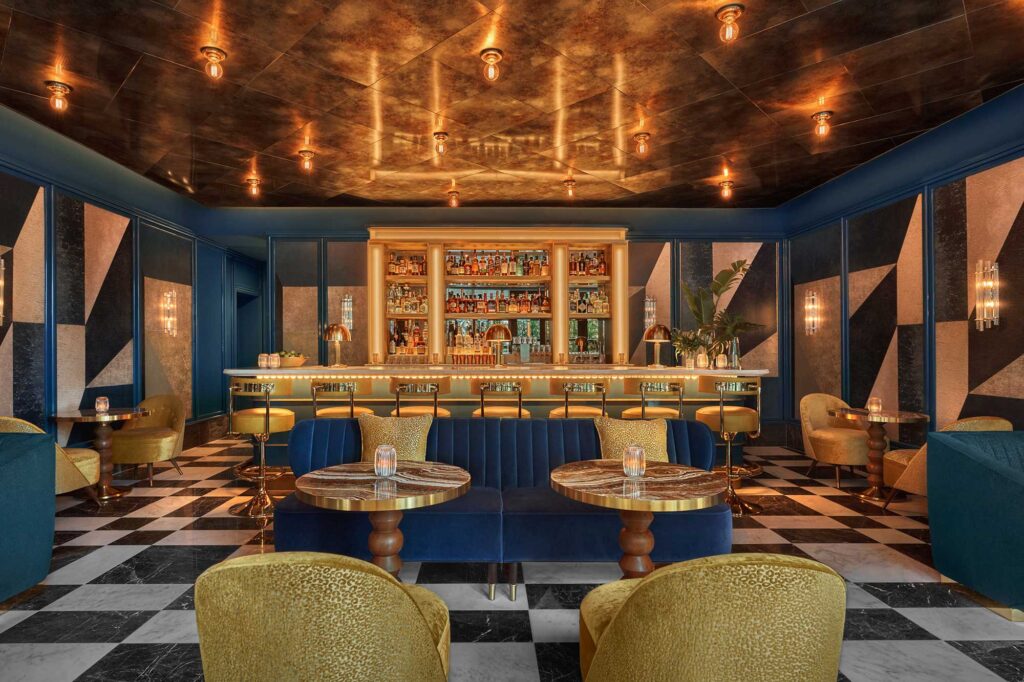 Interior of a fancy bar with dark blue walls, gold accents and black-and-white checkered floors.