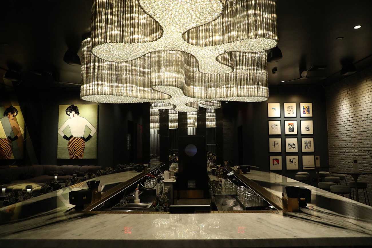 The modern, gray-hued interior of Or Bar in West Hollywood, California, features a large architectural chandelier.