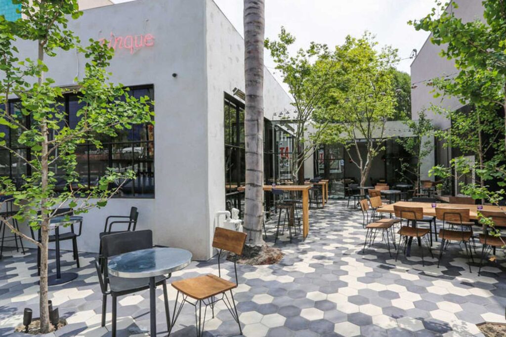 Courtyard restaurant seating featuring oversized hexagon tile in shades of gray and white and several live trees. Zinque, West Hollywood, California.