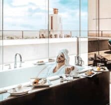 A man wearing a head wrap and cucumber slices on his eyes relaxes in a bathtub at a West Hollywood hotel.