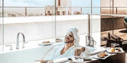 A man wearing a head wrap and cucumber slices on his eyes relaxes in a bathtub at a West Hollywood hotel.