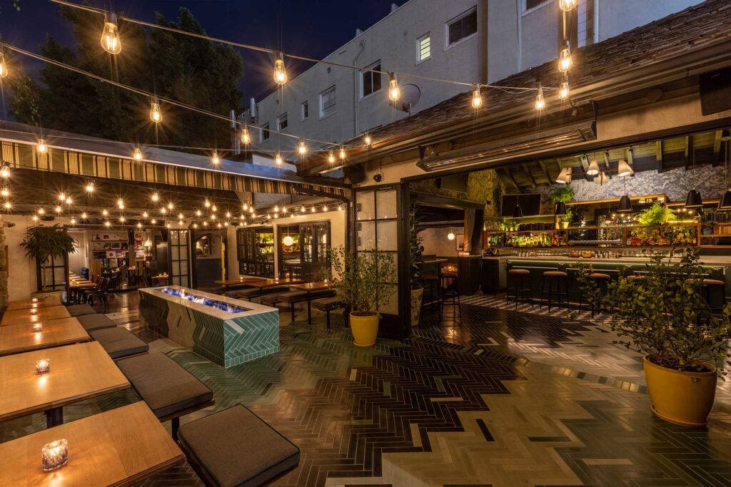 The open-air patio at The Den on Sunset, featuring a large firepit, bench seating and string lights.