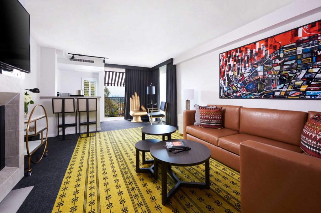 A living room in a suite at the Montrose at Beverly Hills, with a leather sectional, dark wood coffee table, bright yellow rug and other quirky, colorful furnishings.