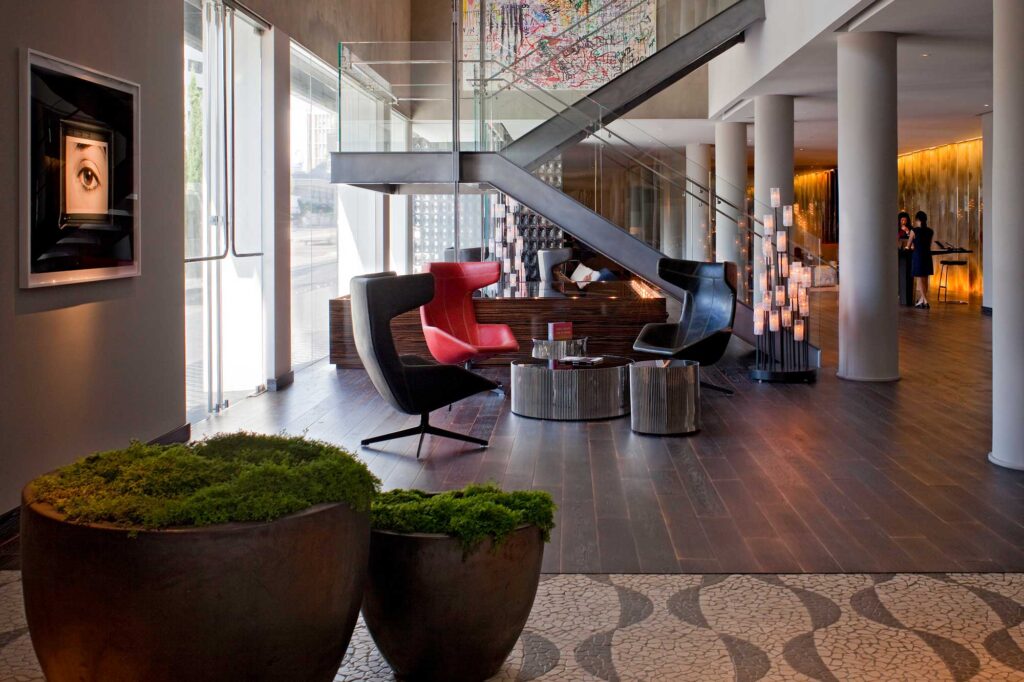 The lobby of the Andaz West Hollywood, with dark wood flooring, modern furnishings and accents, and a huge glass staircase leading to the floors above.