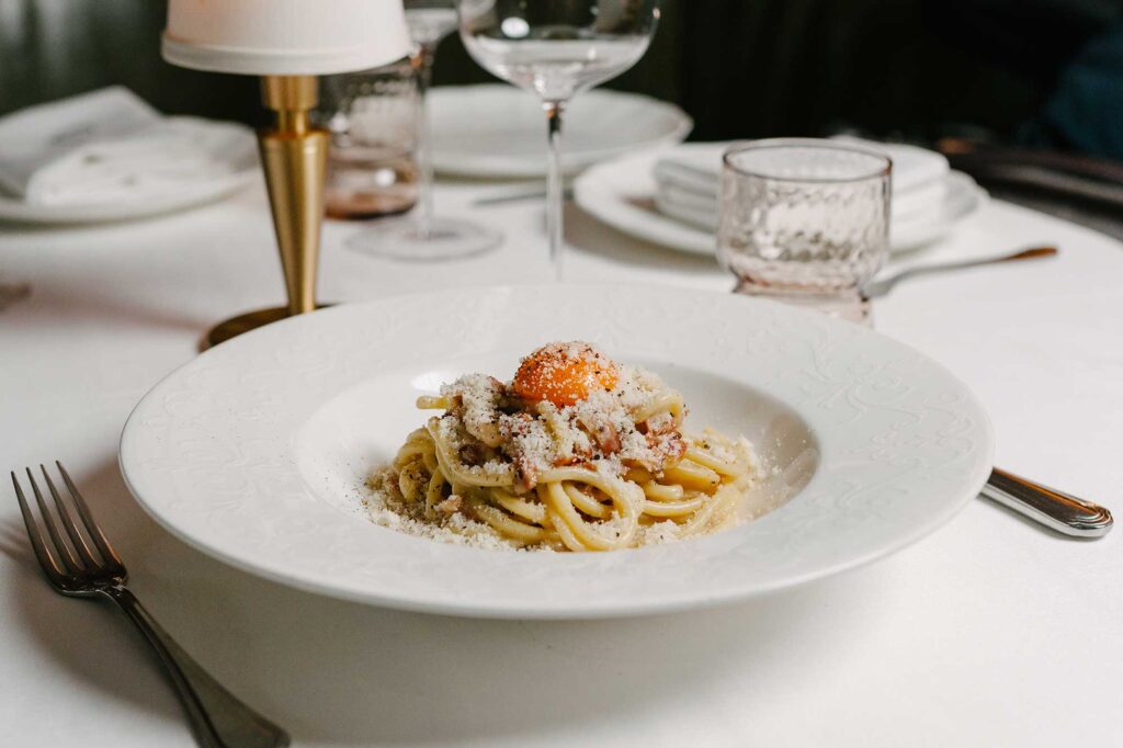 A rich carbonara pasta, with thick noodles, topped with grated parmesan cheese and a beautiful orange egg yolk.