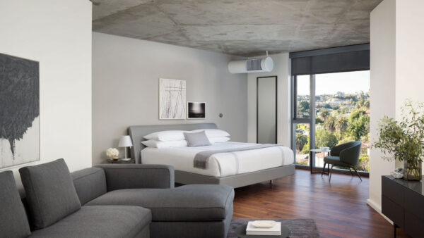 Studio bedroom at AKA West Hollywood, with a king-size bed, separate seating area with sofas and floor-to-ceiling windows overlooking Los Angeles.
