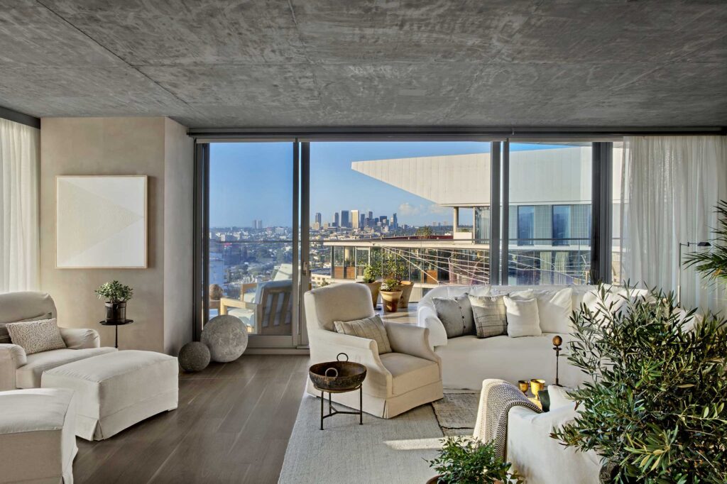 View of the luxurious Canyon House Suite at the 1 Hotel West Hollywood, showing a sitting room with a white sofa and a picture window overlooking downtown Los Angeles. West Hollywood, California.