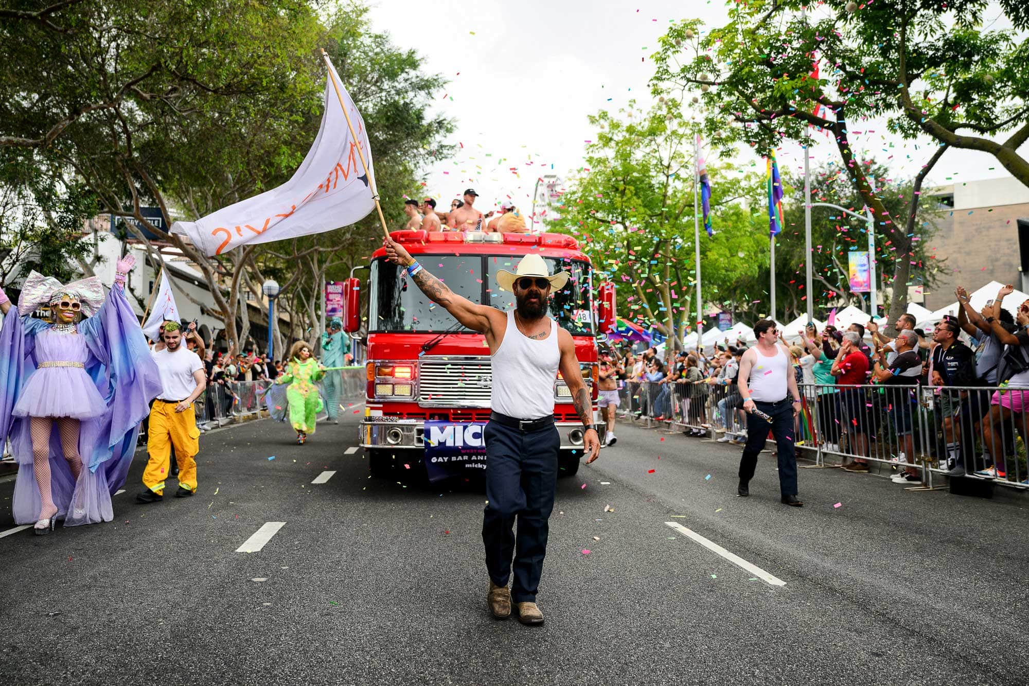 A man wearing a cowboy hat twirls a flag in front of a fire truck during the 2024 WeHo Pride parade.