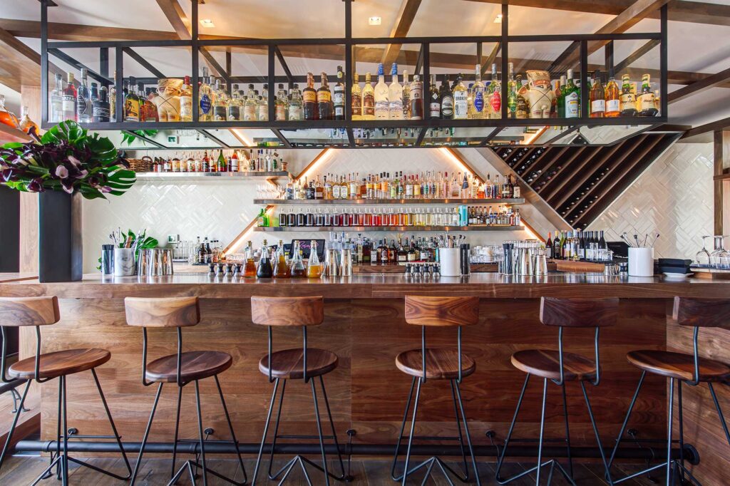 View of the bar area at Rosaline in West Hollywood, California, featuring a wooden bar and colorful bottles on the back wall.
