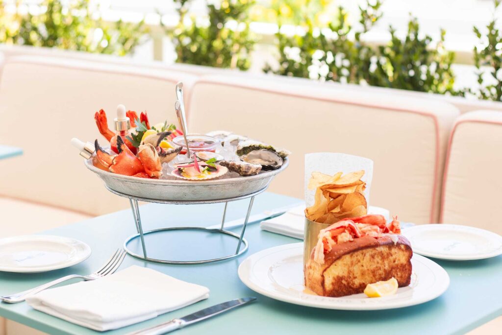 A seafood platter and lobster roll sit on an outdoor patio table at Saltie Girl in West Hollywood, California.