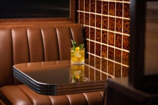 A yellow-hued cocktail sits on a tabletop in a leather booth at Bar Next Door, West Hollywood, California.