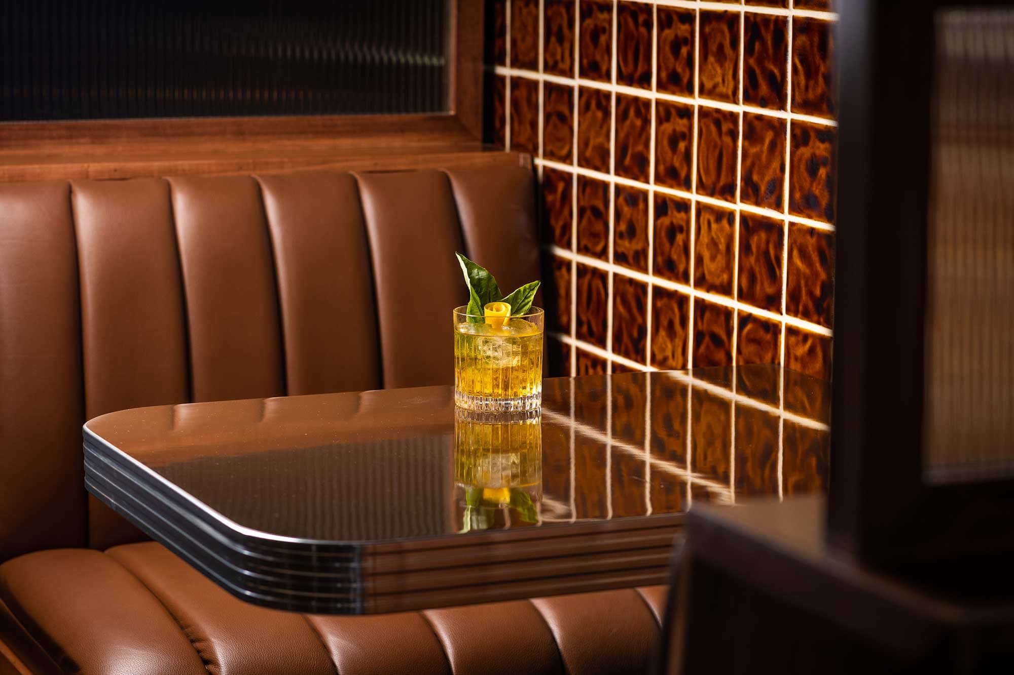 A yellow-hued cocktail sits on a tabletop in a leather booth at Bar Next Door, West Hollywood, California.