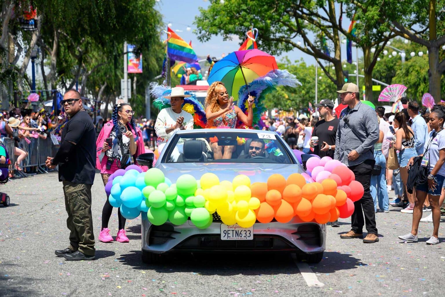 A vintage car decorated with rainbow-colored balloons drives in the WeHo Pride Parade.