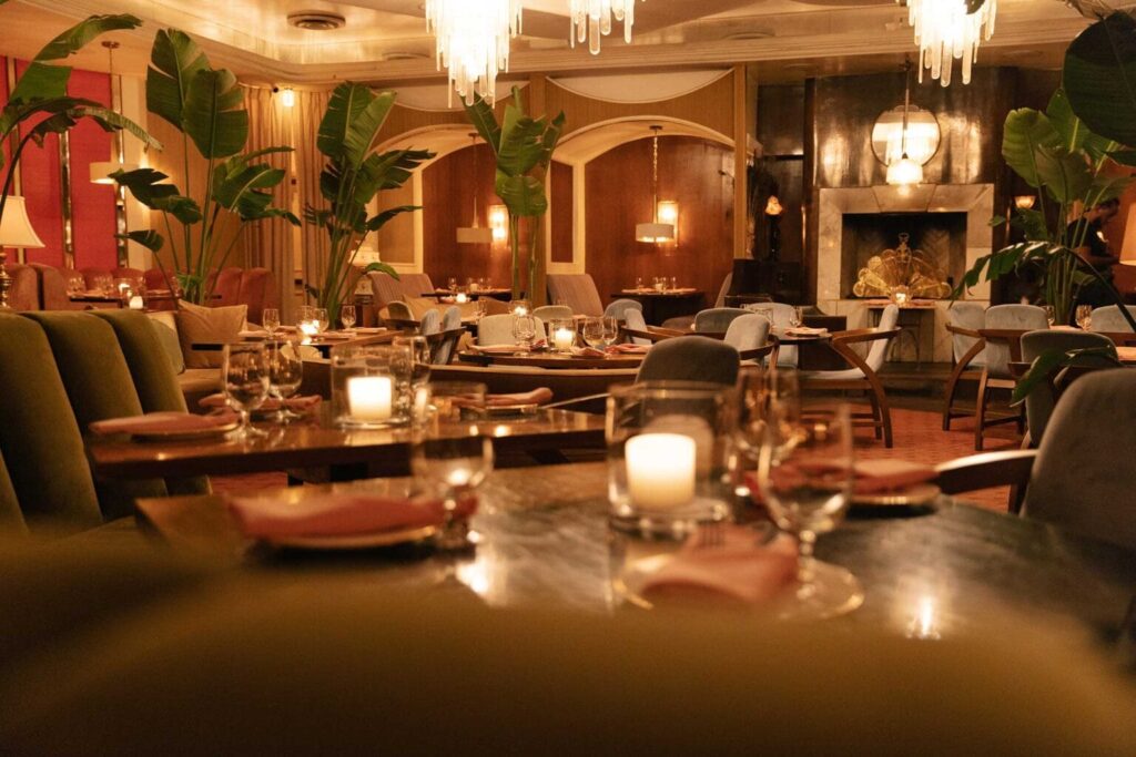 Interior of Delilah in West Hollywood, CA, with retro decor, set tables, candles, tall green plants and chandeliers overhead.