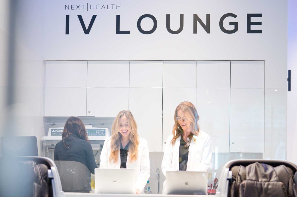 Two women stand with laptops at the IV Lounge at Next Health in West Hollywood, California.