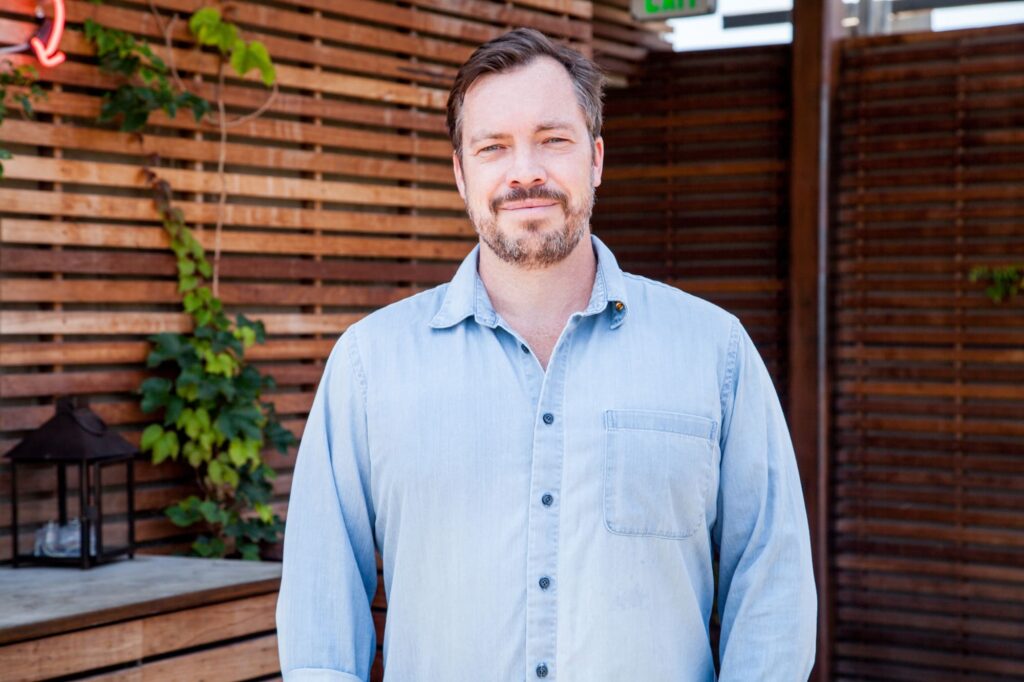 Headshot of restaurateur David Combes wearing a denim button-up shirt.