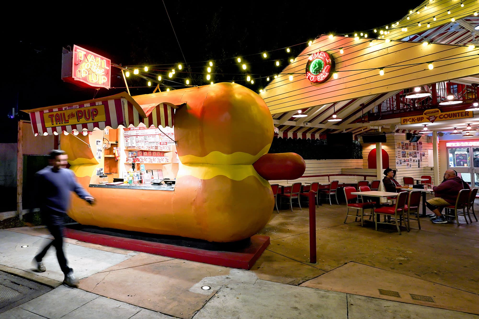 A man walks by the Tail O' the Pup hot dog stand in West Hollywood at night
