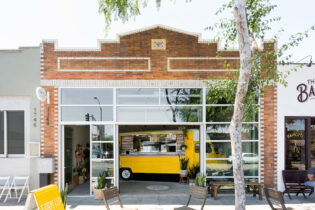 The exterior of Farm Cup Coffee features a glass garage door holding a yellow vintage food truck.