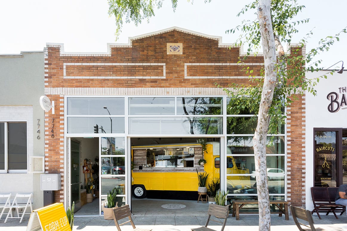The exterior of Farm Cup Coffee features a glass garage door holding a yellow vintage food truck.