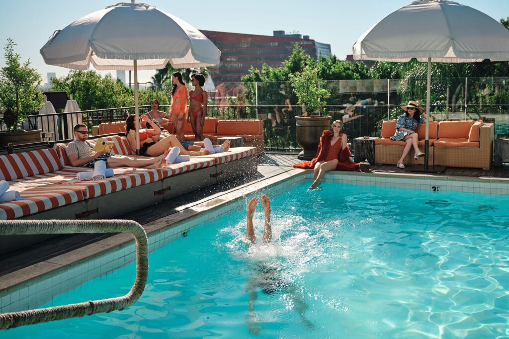 People relaxing by the poolside with umbrellas and lounge chairs in West Hollywood, California, during a sunny day.