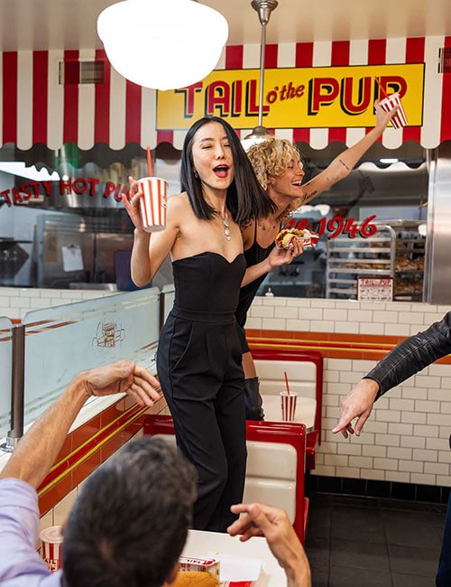A woman stands on a booth as her friends cheer on at Tail O' the Pup in West Hollywood.