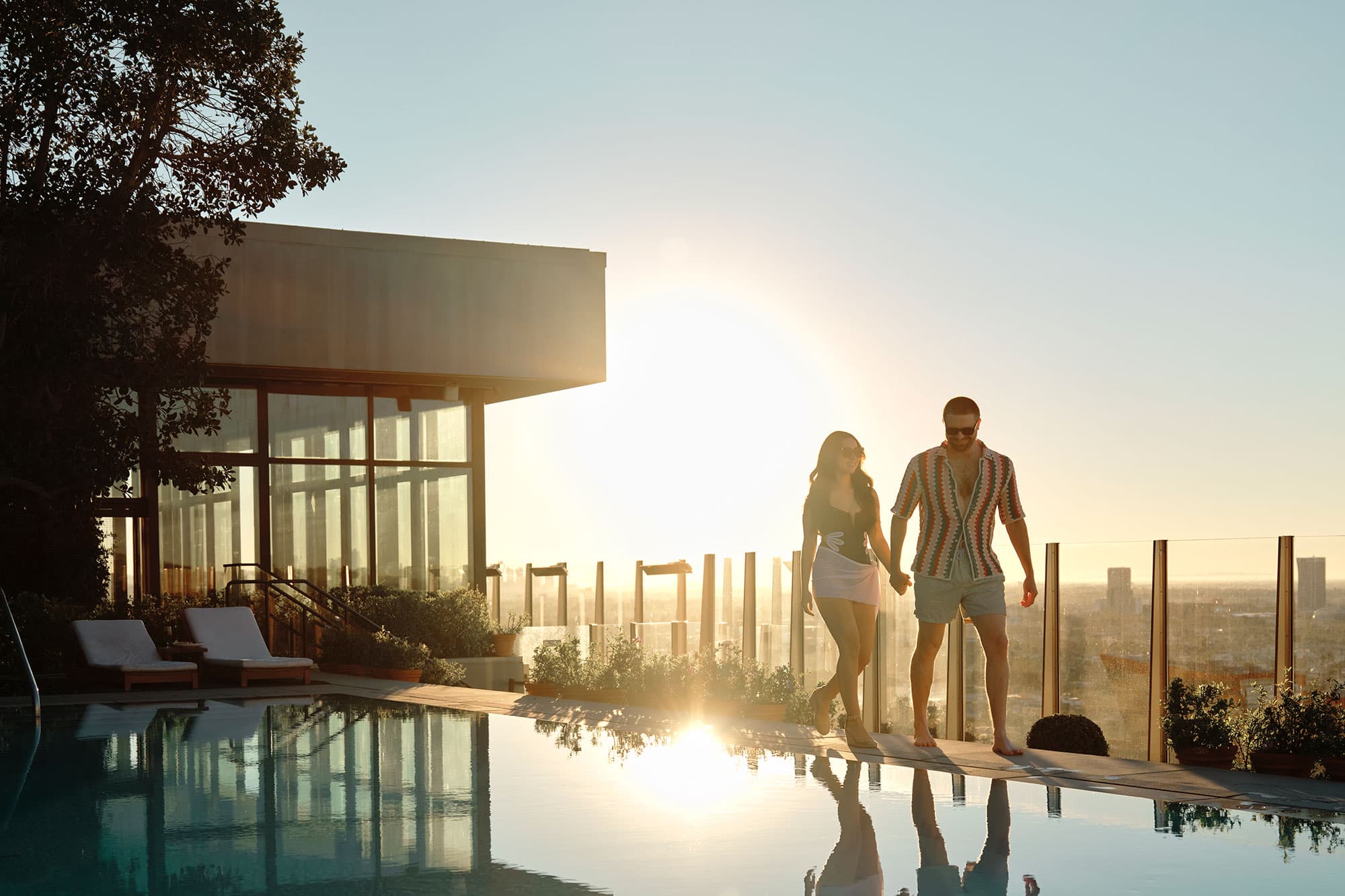 A couple walks along a rooftop pool in West Hollywood at sunset.