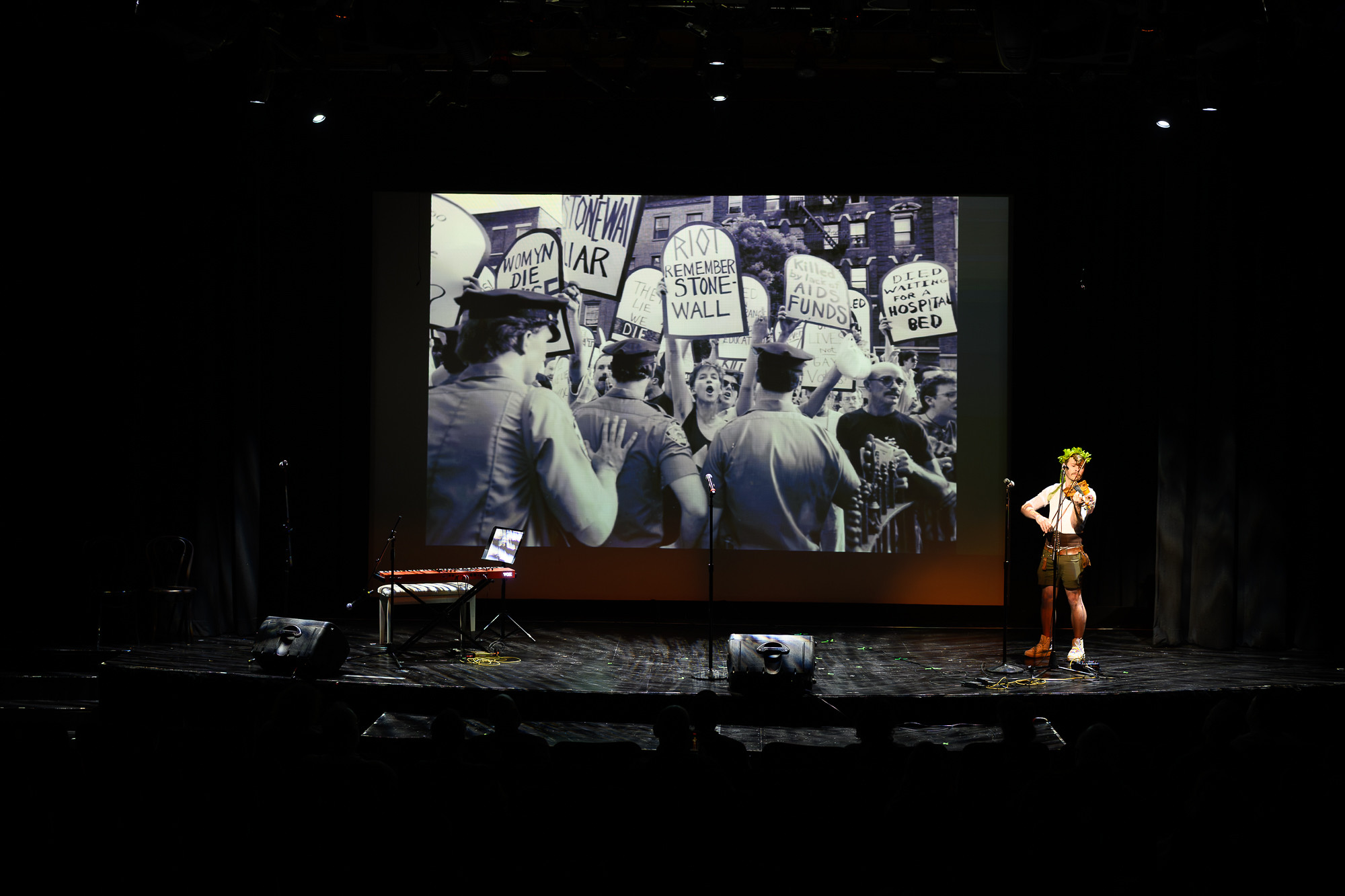 A performer on stage amid a backdrop of historical LGBTQ+ images at the WeHo Pride Arts Festival