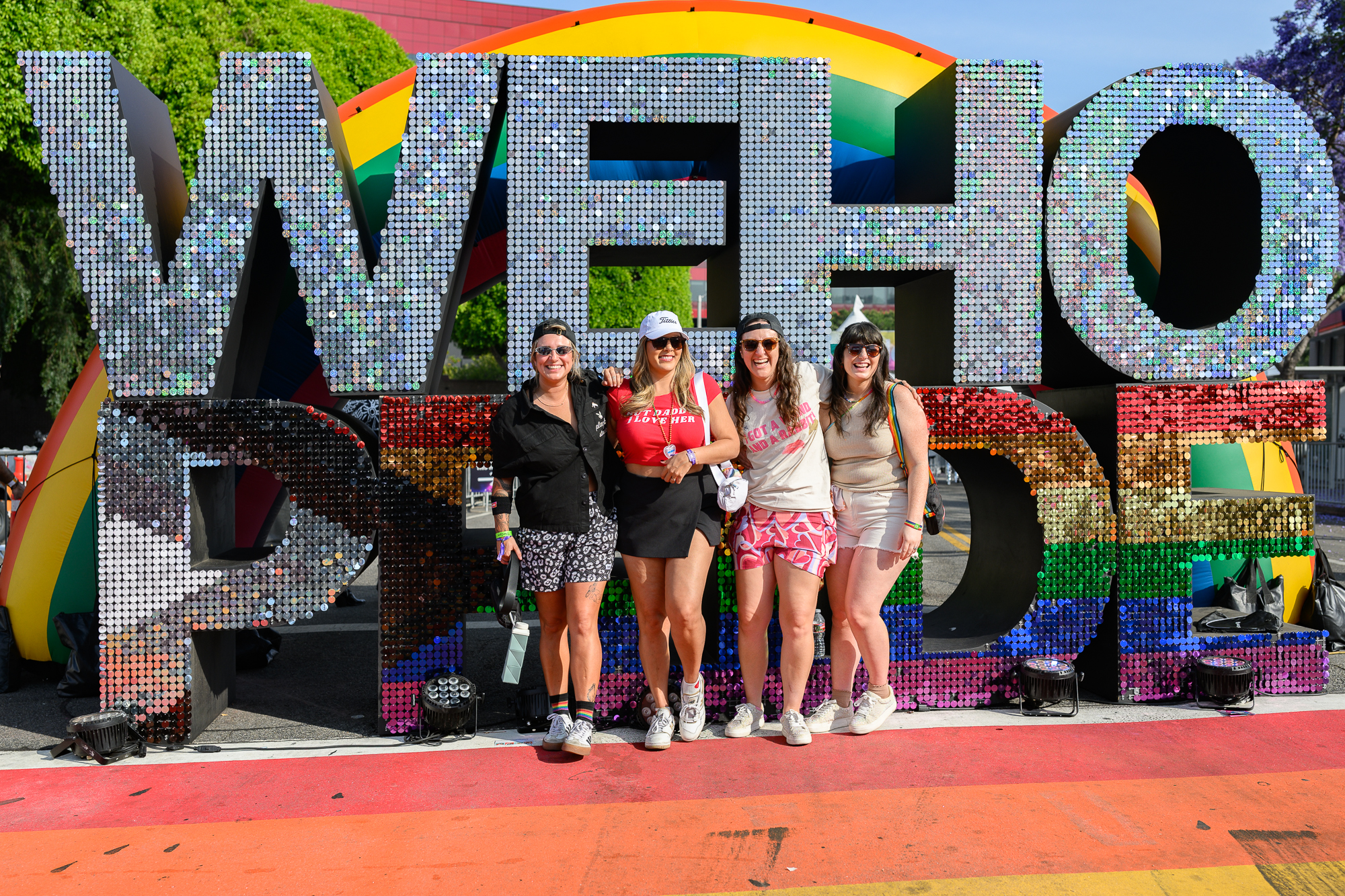 People stand in front of a glittery sign reading "WeHo Pride"