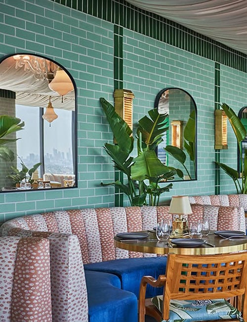 Interior of The Rooftop at The Sun Rose restaurant in West Hollywood, California, featuring colorful tiled walls, draped ceilings and rounded booths.