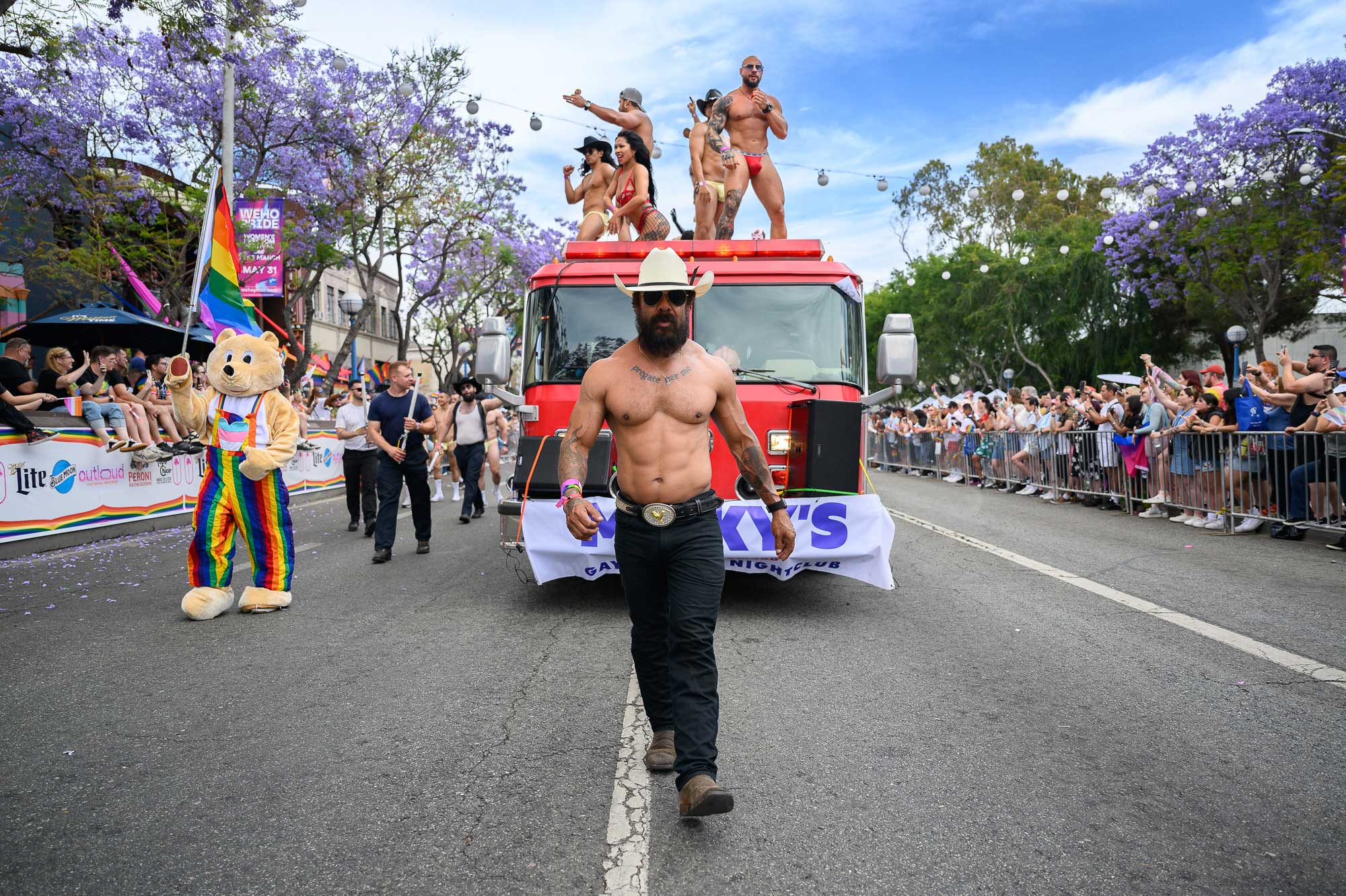 A firetruck carrying male go-go dancers from Micky's bar, along with a shirtless man walking ahead, participates in the WeHo Pride festival.