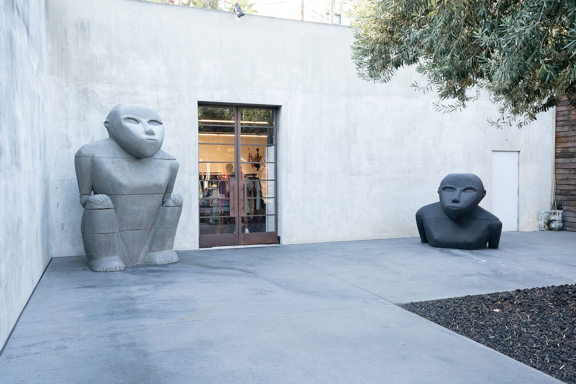 Two large abstract humanoid sculptures sit near a glass door on a concrete patio at Maxfield in West Hollywood, CA.