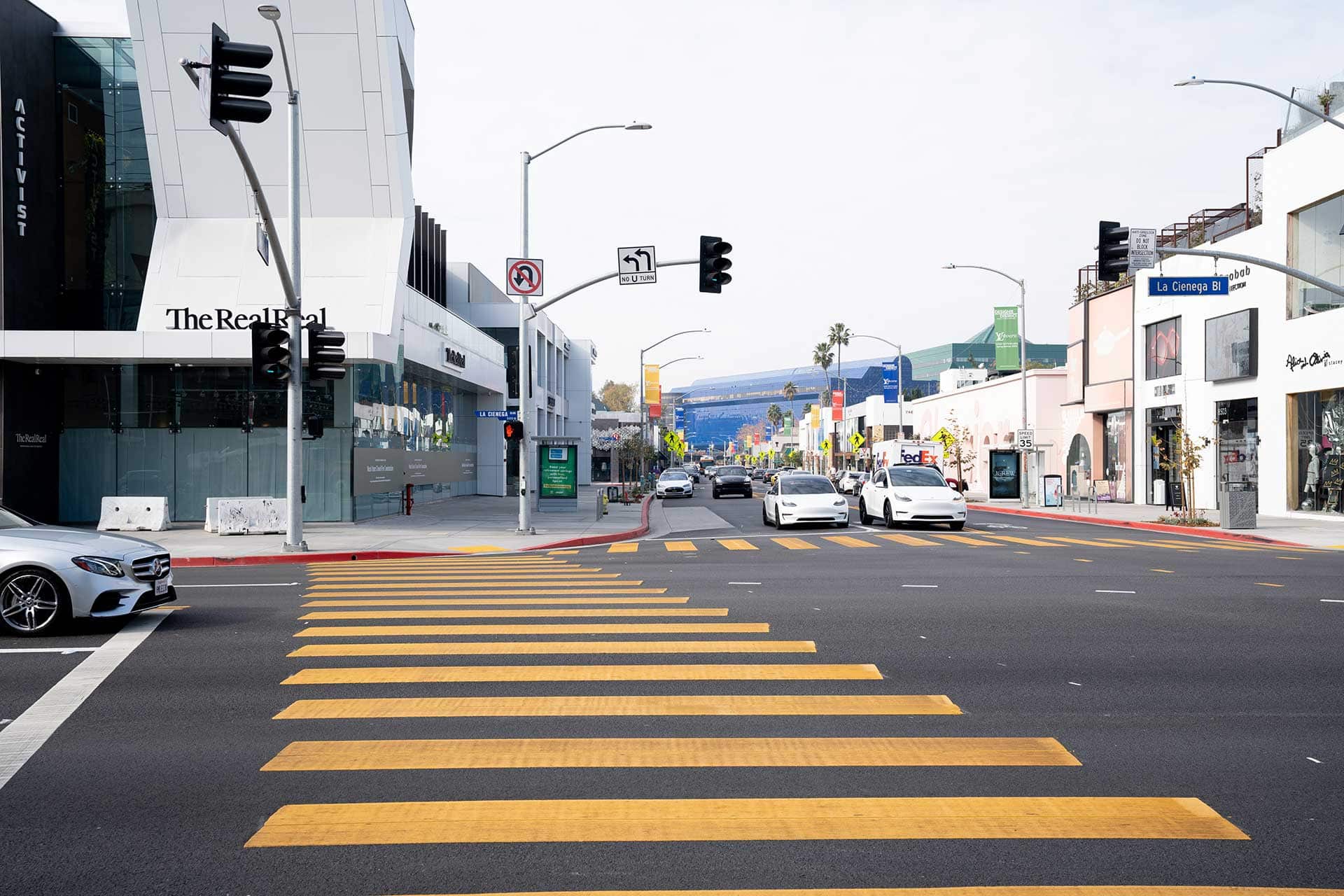 The intersection of Melrose and La Cienega boulevards in West Hollywood, with cars waiting at a red light and storefronts lining both sides.