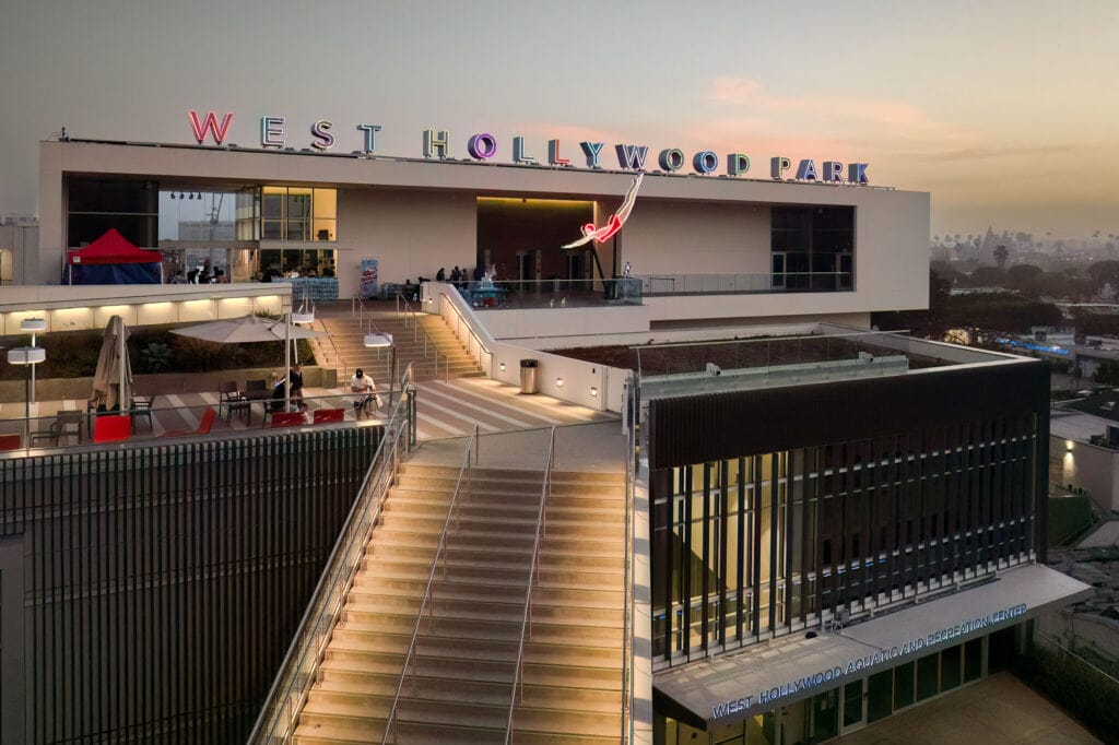 A modern building at sunset with “West Hollywood Park” sign, outdoor stairs, and people sitting on terraces.